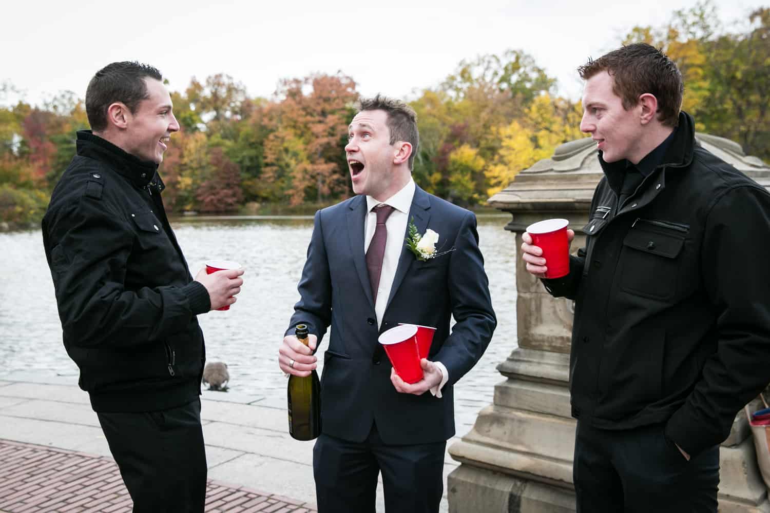 Groom celebrating with two male guests at a Bethesda Fountain wedding in Central Park