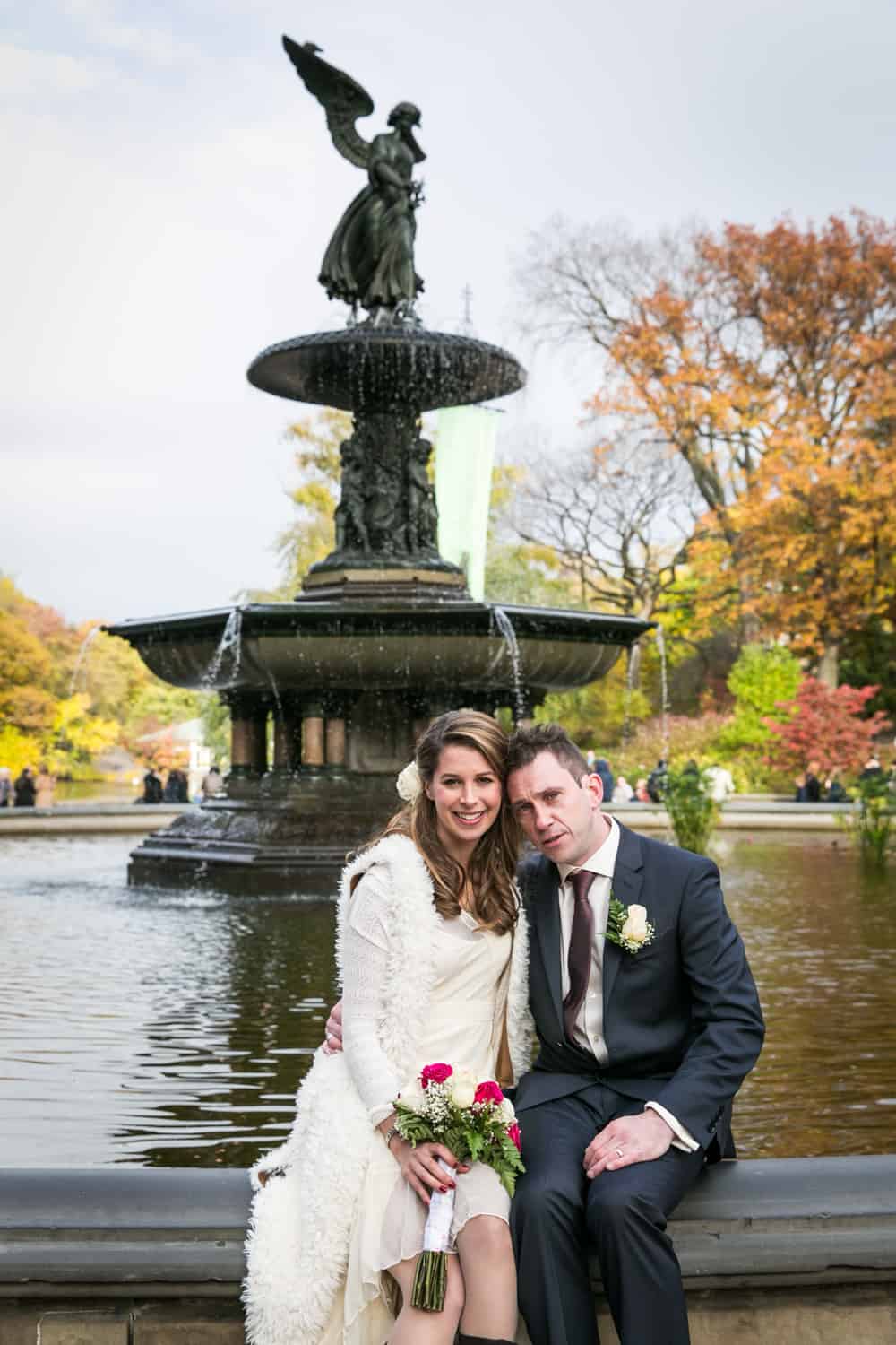 Bride and groom sitting in front of Bethesda Fountain