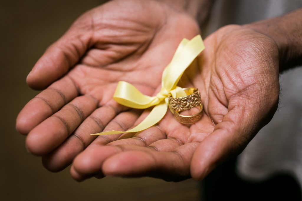 Close up of African American hands holding a set of wedding rings with yellow ribbon
