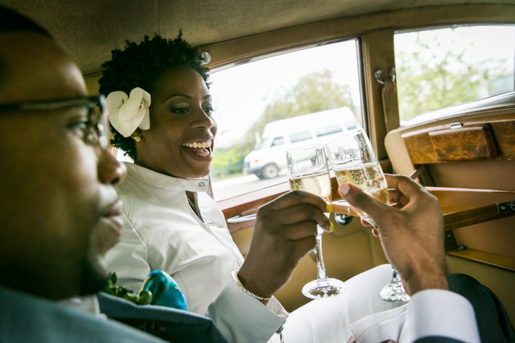 Bride and groom toasting with champagne in the back seat of a car