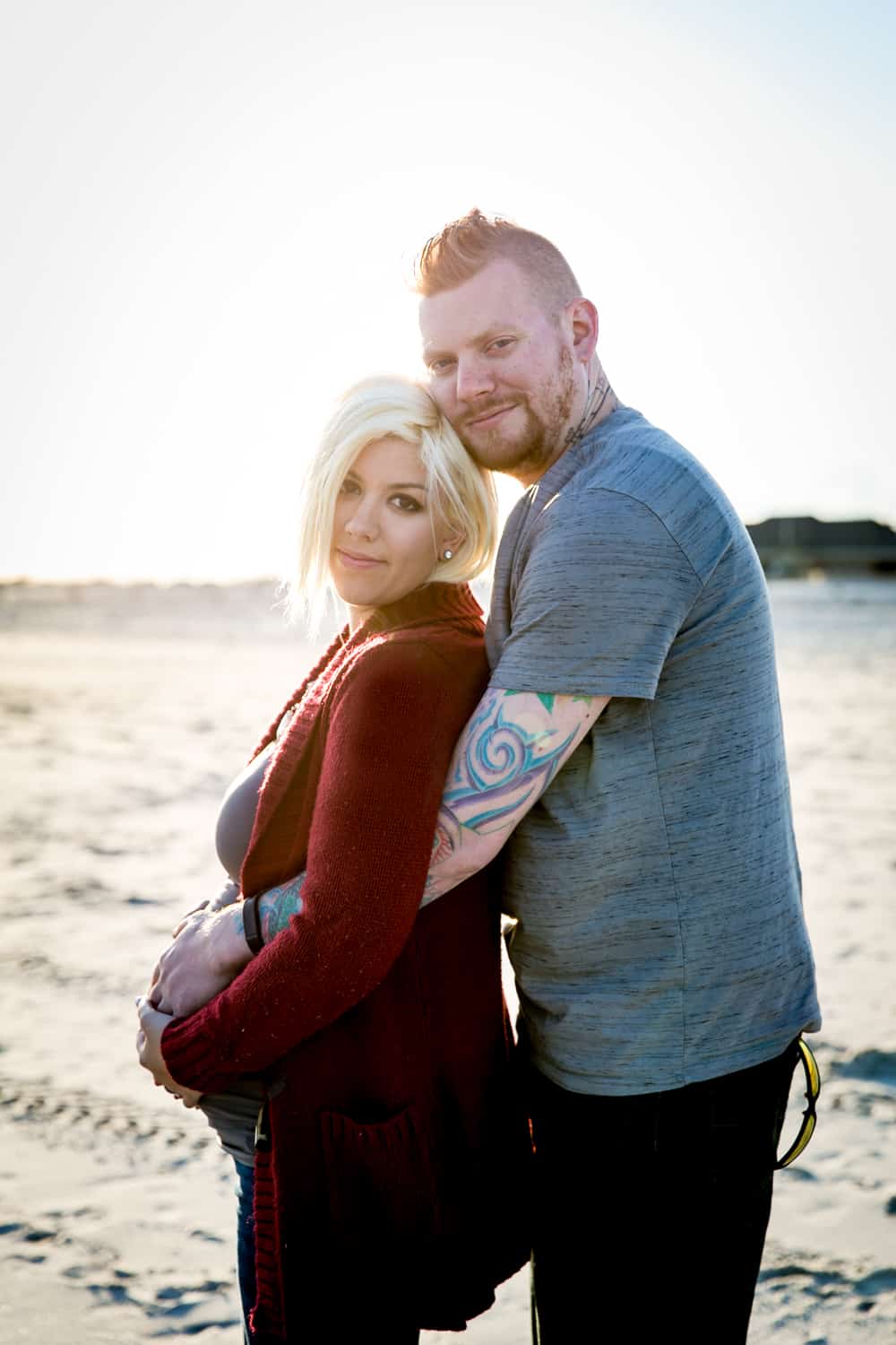 Pregnant blond woman and partner on beach for an article on how to prepare for a maternity photo shoot