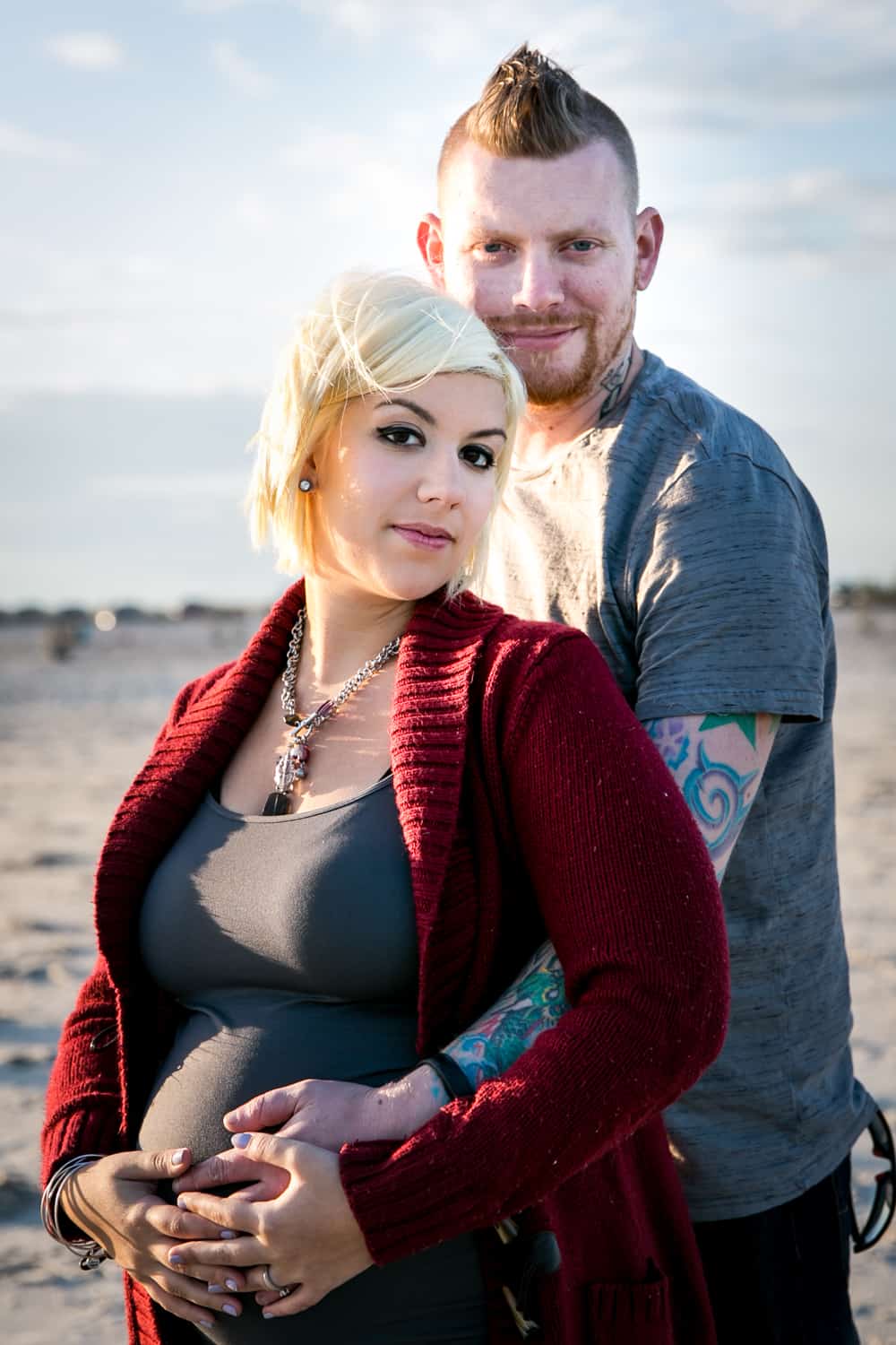 Pregnant blond woman and partner on beach for an article on how to prepare for a maternity photo shoot