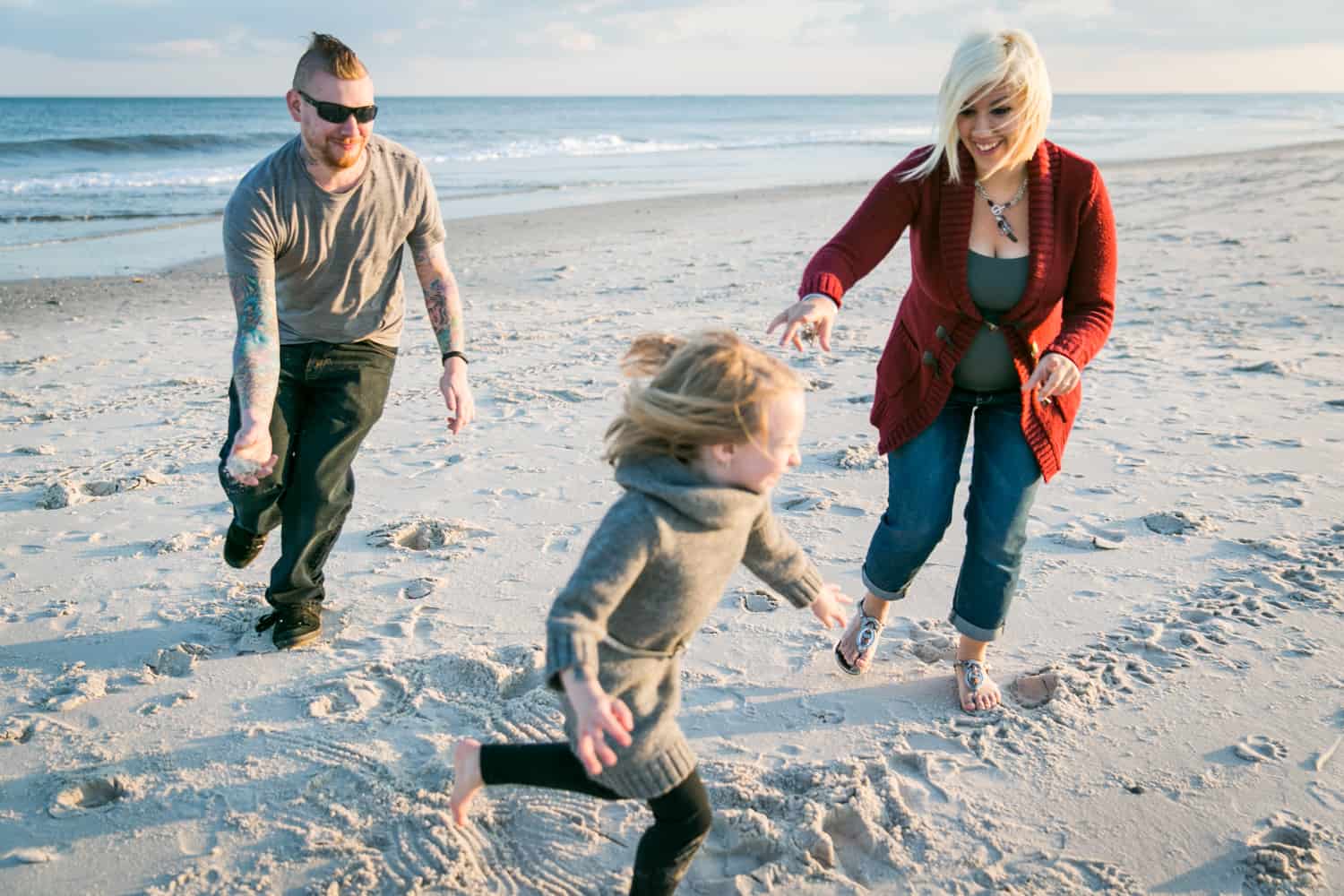 Father and mother chasing little girl on beach