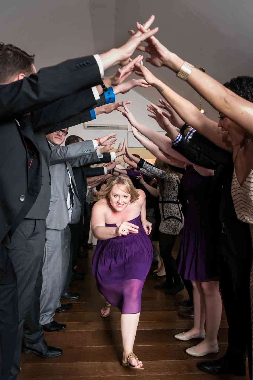 Female guest wearing purple dress running under arch of other guests' arms