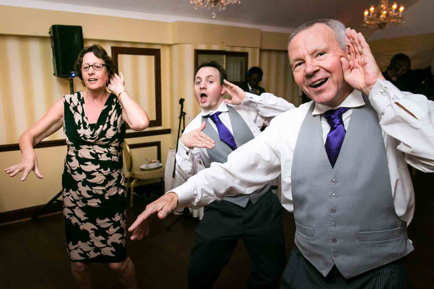 Three guests dancing at wedding reception with arms outstretched