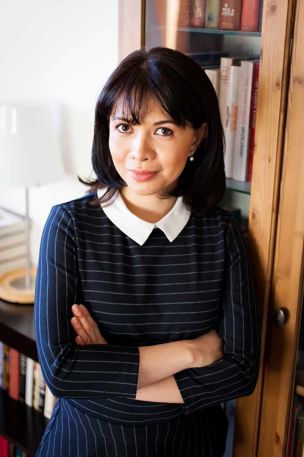 Woman leaning against bookshelf wearing pinstripe blouse for an article on online portrait tips