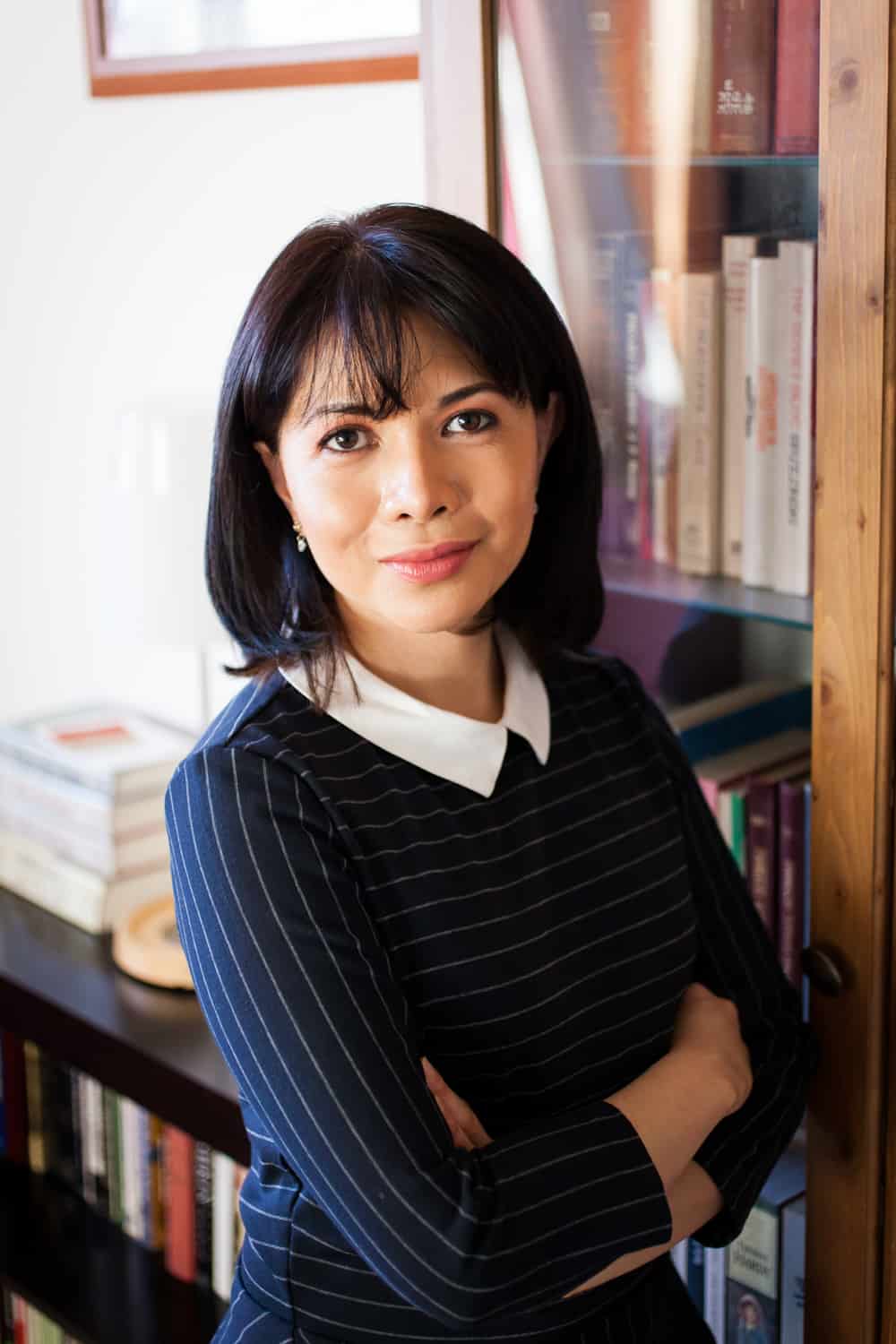 Woman leaning against bookshelf wearing pinstripe blouse for an article on online portrait tips