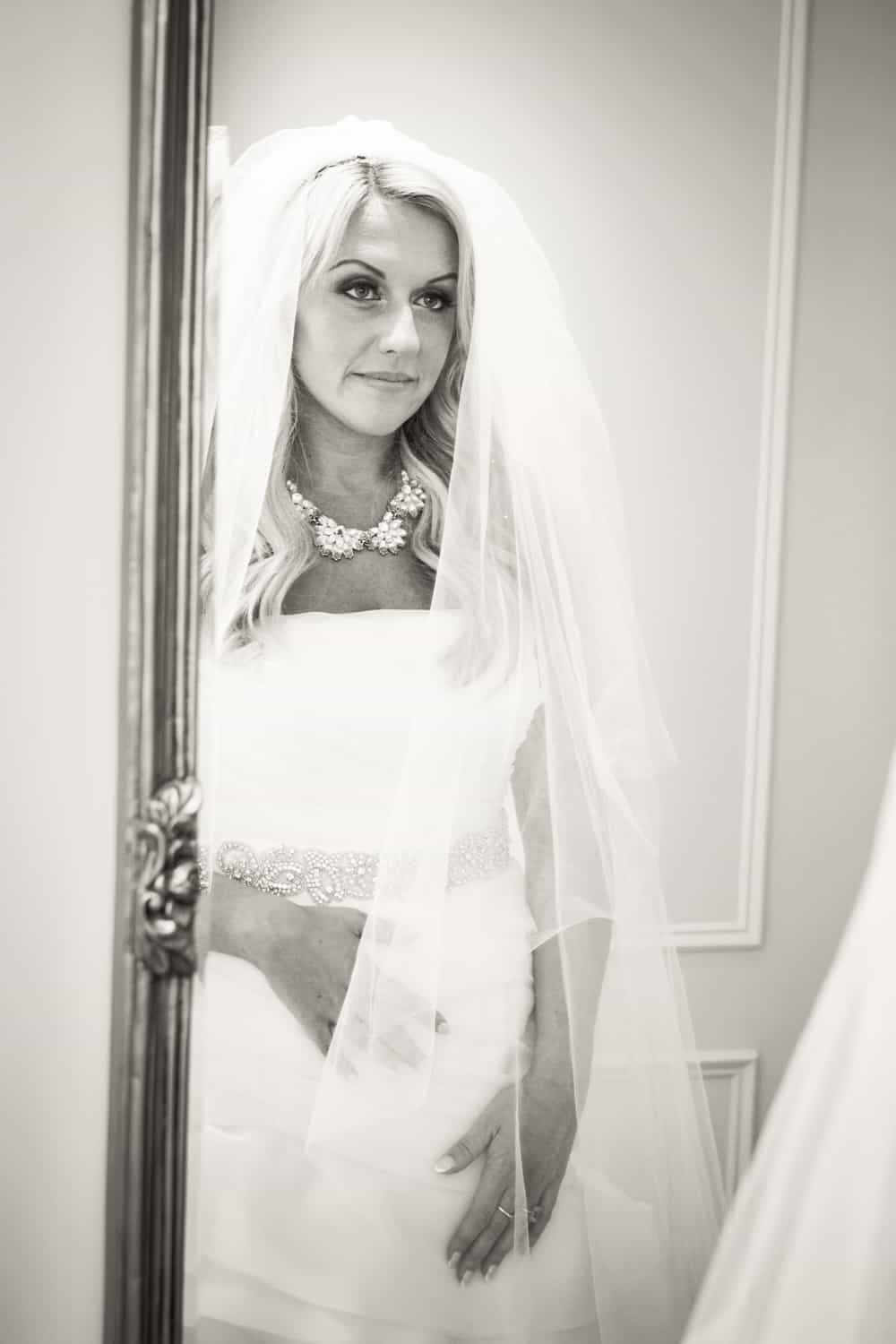 Black and white photo of bride looking at herself in mirror