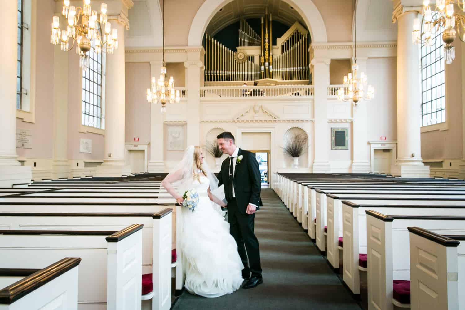 Bride and groom leaning against pews in All Souls Unitarian Church