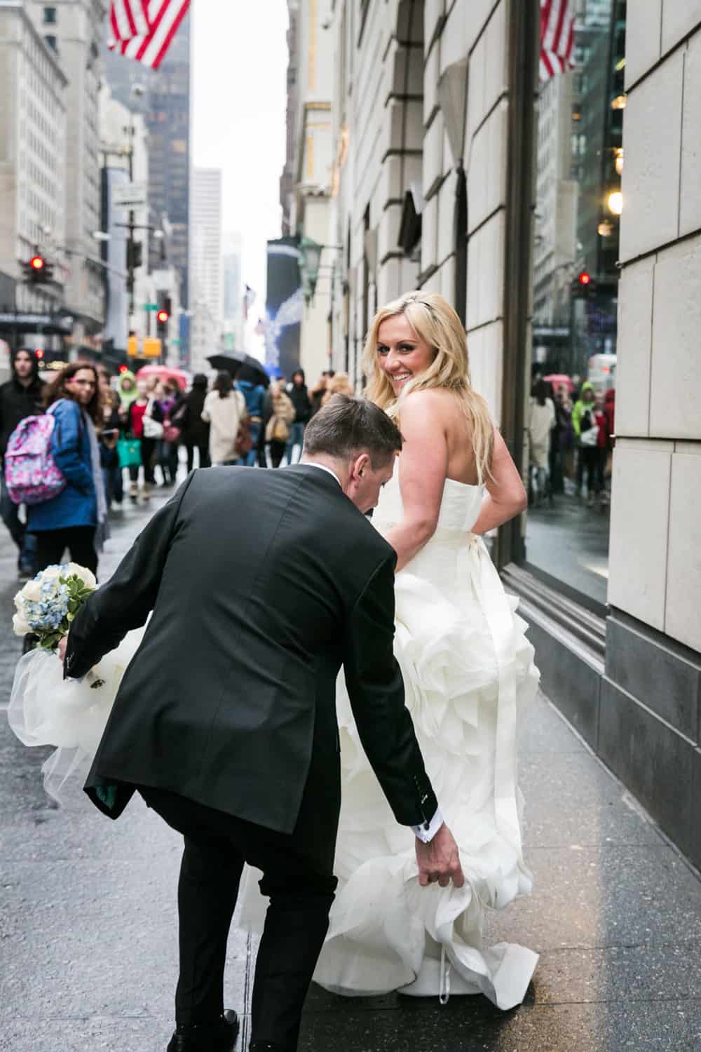 Groom helping bride with dress on NYC sidewalk