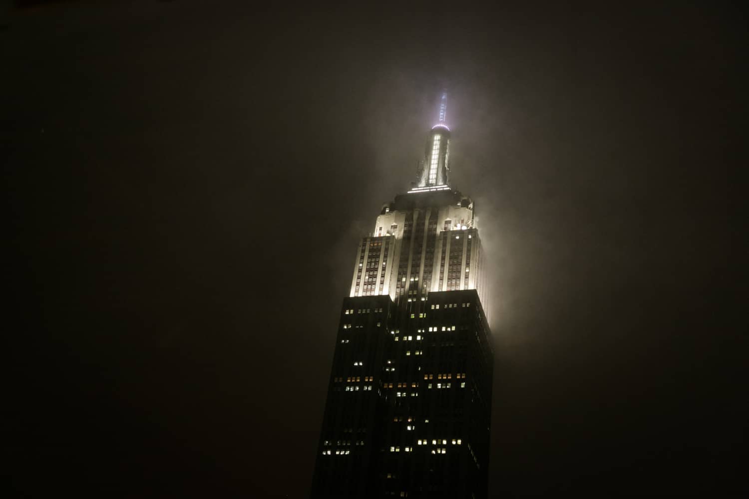Top of the Empire State Building shrouded in fog at night