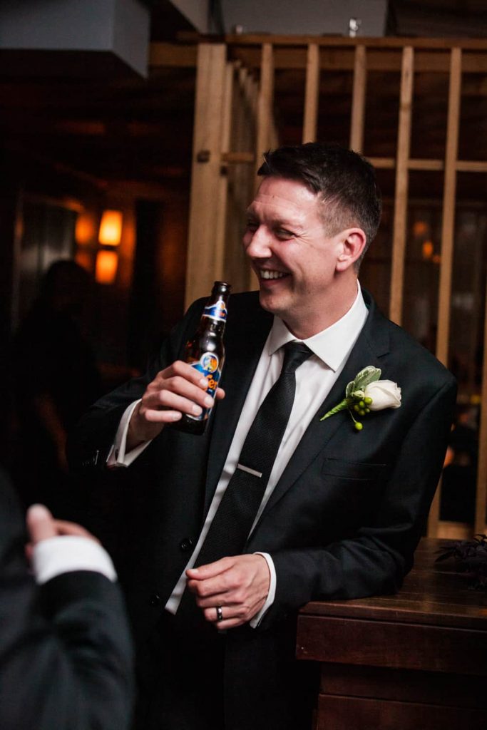 Groom drinking bottle of beer at a Bergdorf Goodman wedding reception