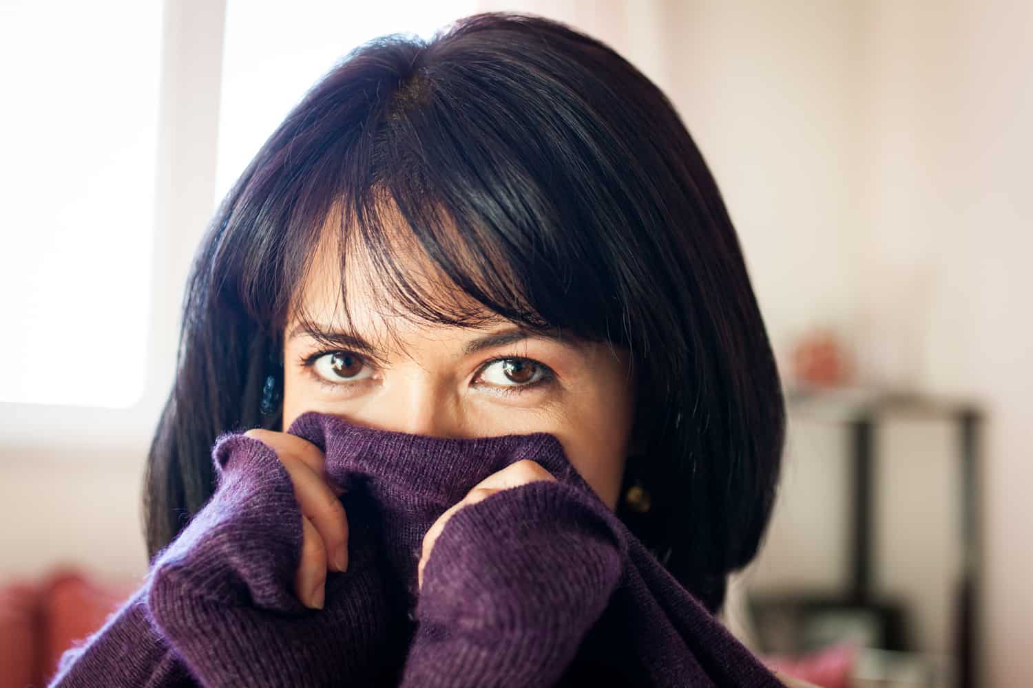 Woman with short black hair holding sweater in front of her face for an article on how to look slimmer in photos