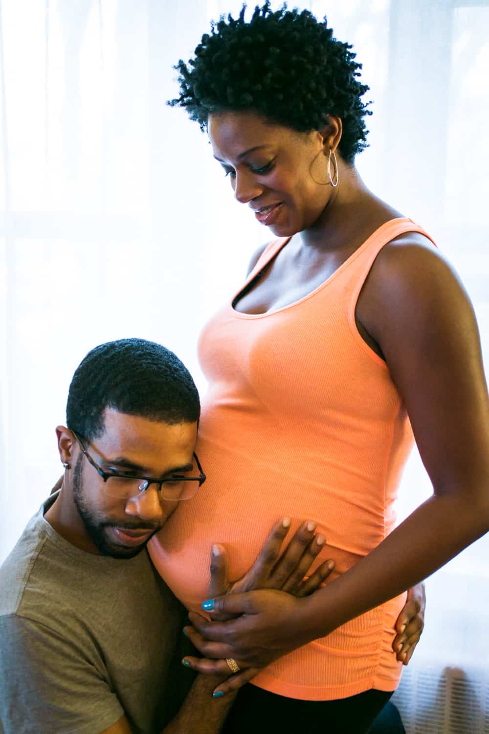 Father-to-be listening to pregnant woman's stomach for a Queens maternity photo shoot
