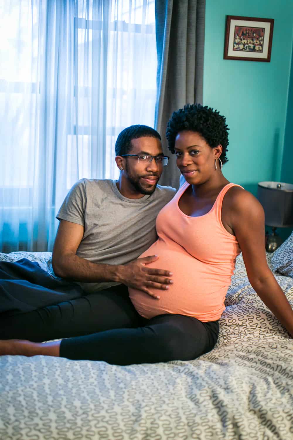 Parents-to-be sitting on bed by Queens maternity photographer