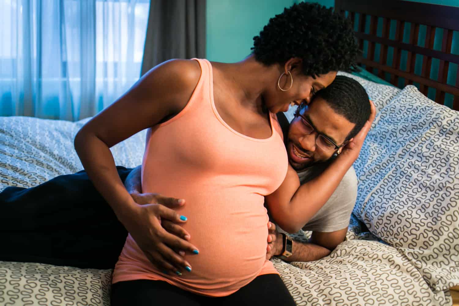 Parents-to-be sitting on bed by Queens maternity photographer
