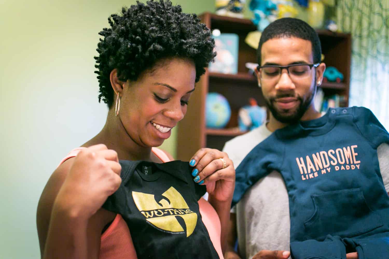 Parents-to-be looking at baby clothes for a Queens maternity photo shoot