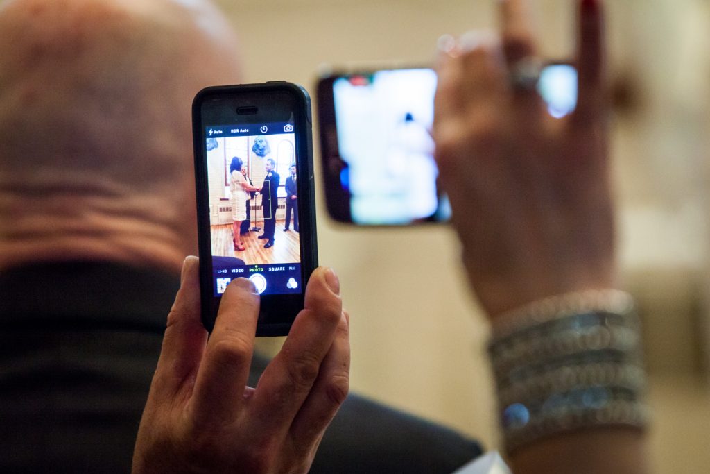 Close up of two cell phones capturing bride and groom at an Alger House wedding ceremony