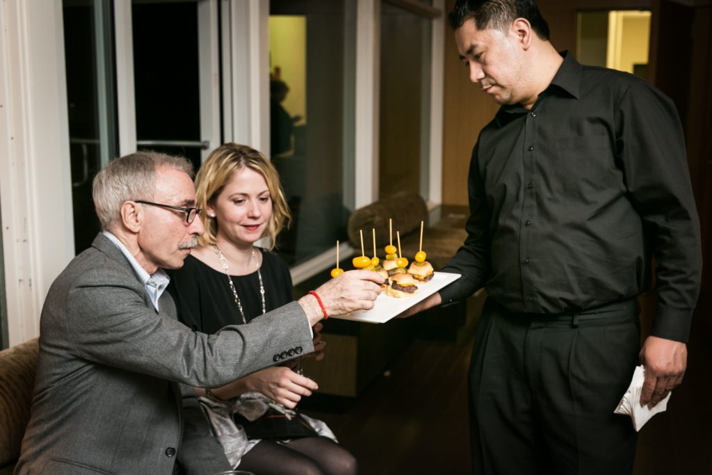 Birthday party photos of couple selecting mini hamburger from appetizer tray