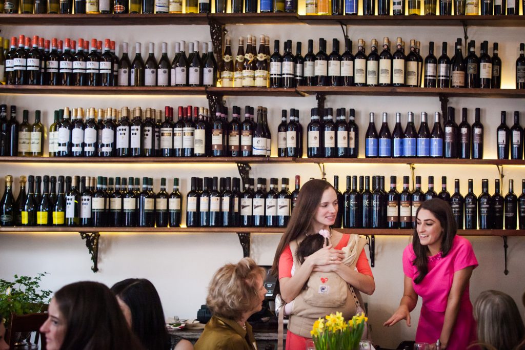 Two women talking with wall of wine bottles in the background