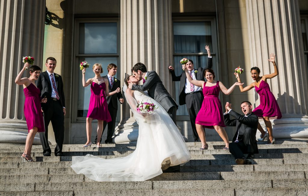 Bride and groom kissing on steps in front of cheering bridal party