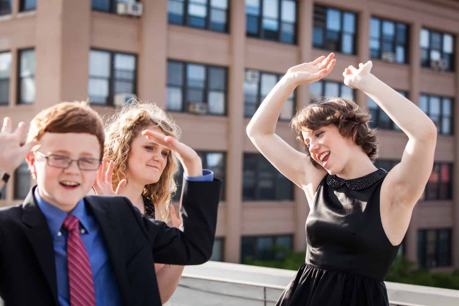 Two girls and one boy dancing with arms raised on roof