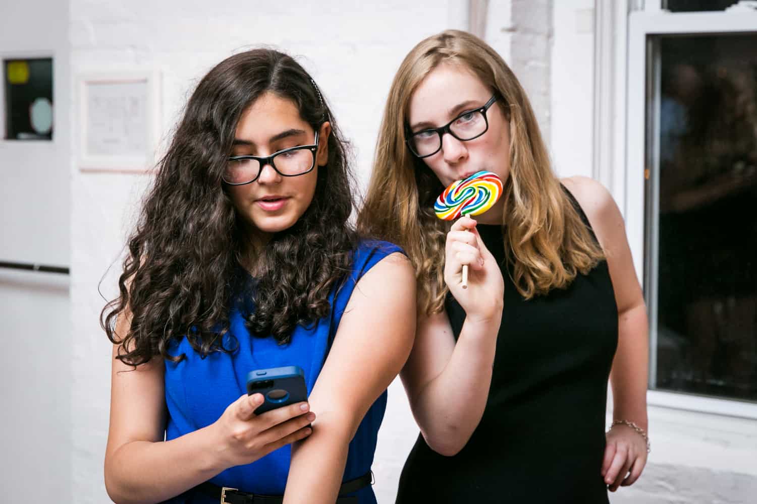 Girl with cell phone and girl licking lollipop for an article on how to plan the perfect bar mitzvah