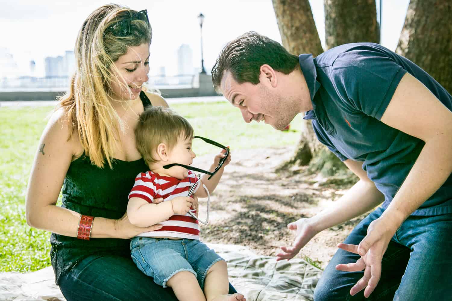 Father playing with baby wearing sunglasses during a Battery Park family portrait