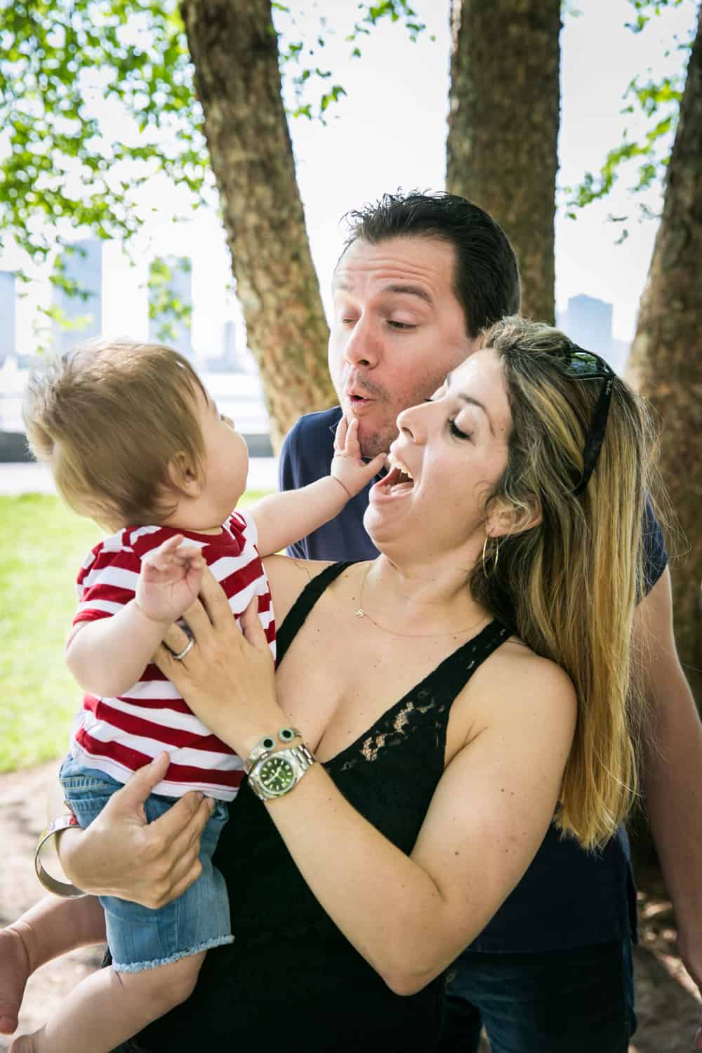 Parents playing with baby beside tree during a Battery Park family portrait