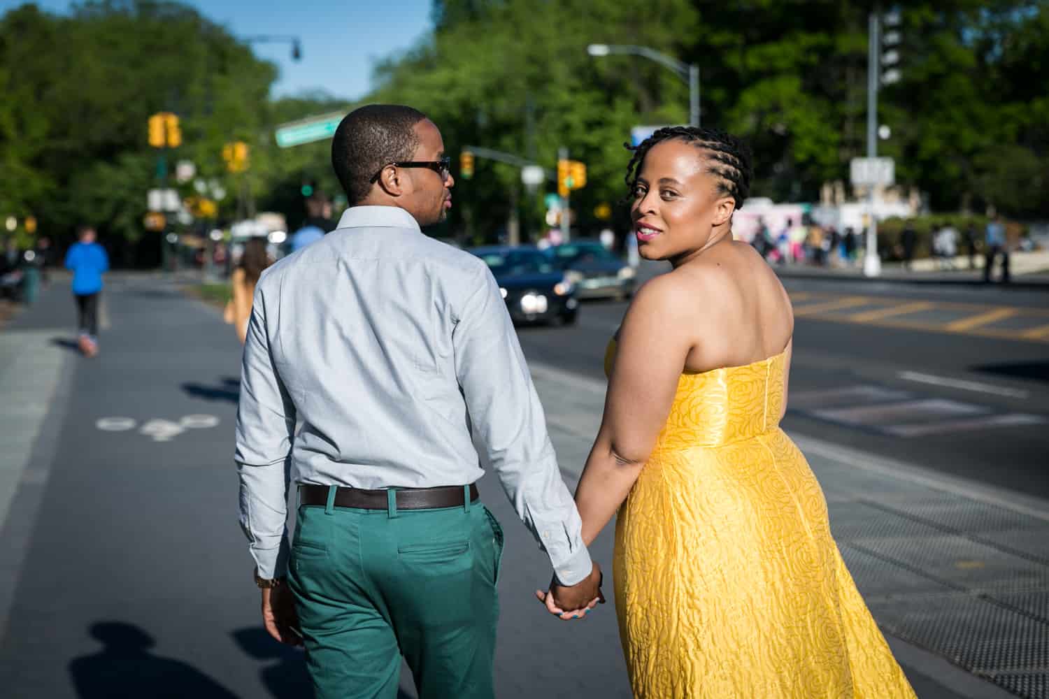 Couple holding hands and walking down sidewalk and woman looking over shoulder