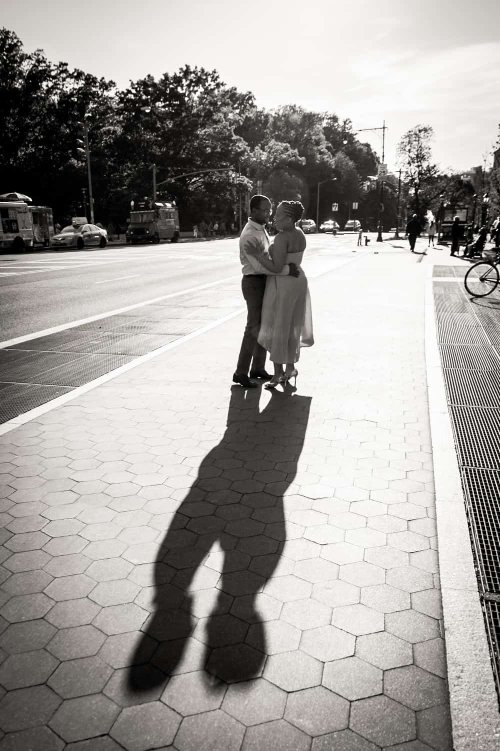 Black and white photo of couple kissing on sidewalk and resulting shadow