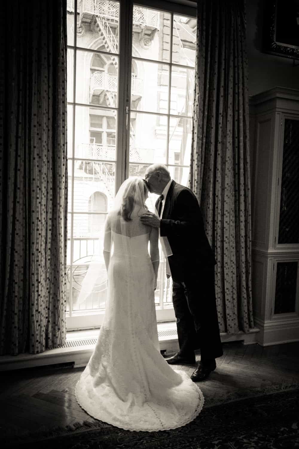 Black and white photo of father kissing bride in front of window before a Harvard Club wedding