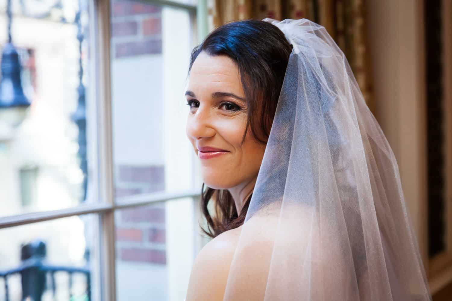 Bride looking over shoulder by a window for an article on the mysteries of photo editing