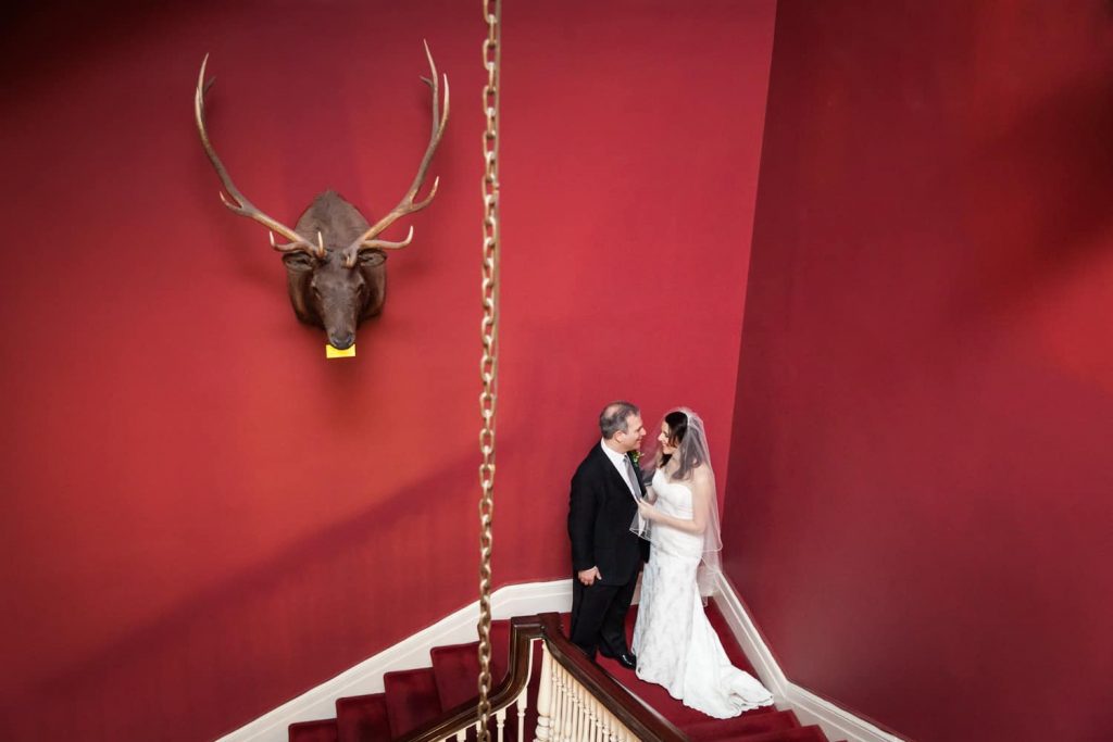 Bride and groom in corner of staircase with moose head on wall before a Harvard Club wedding