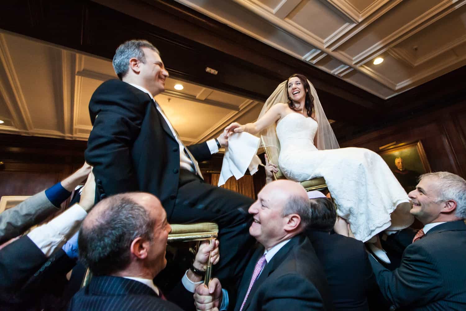 Bride and groom up on chairs during hora dance at Harvard Club wedding