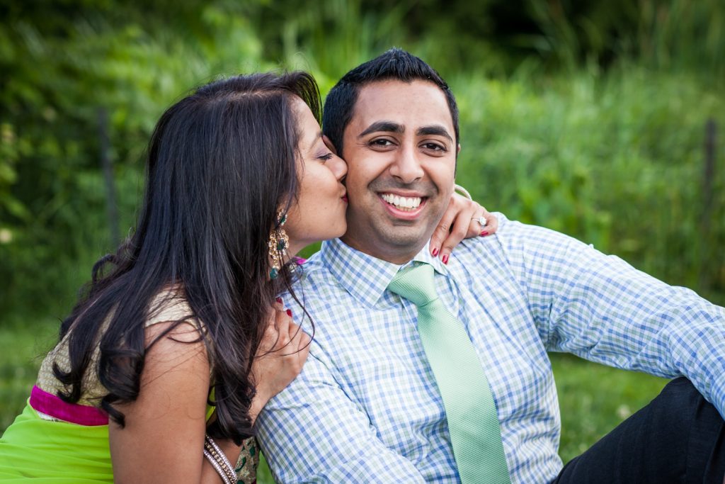 Woman kissing man on cheek in Central Park for an article on NYC engagement shoot ideas