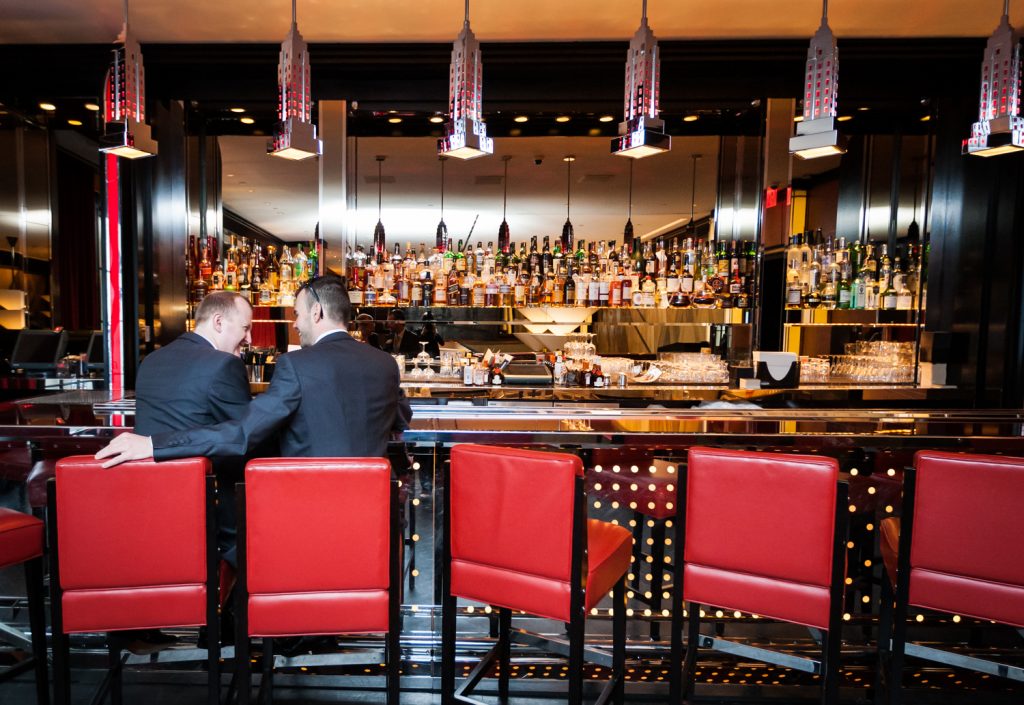 Two grooms sitting in red seats at a Chatwal Hotel bar