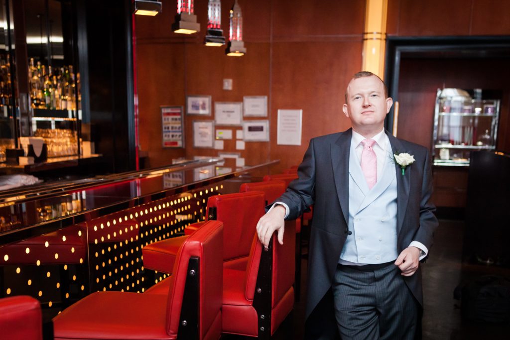 Groom holding on to red chair in Chatwal Hotel bar