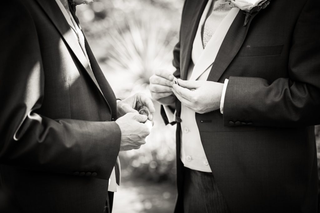 Black and white close up of two grooms holding wedding rings