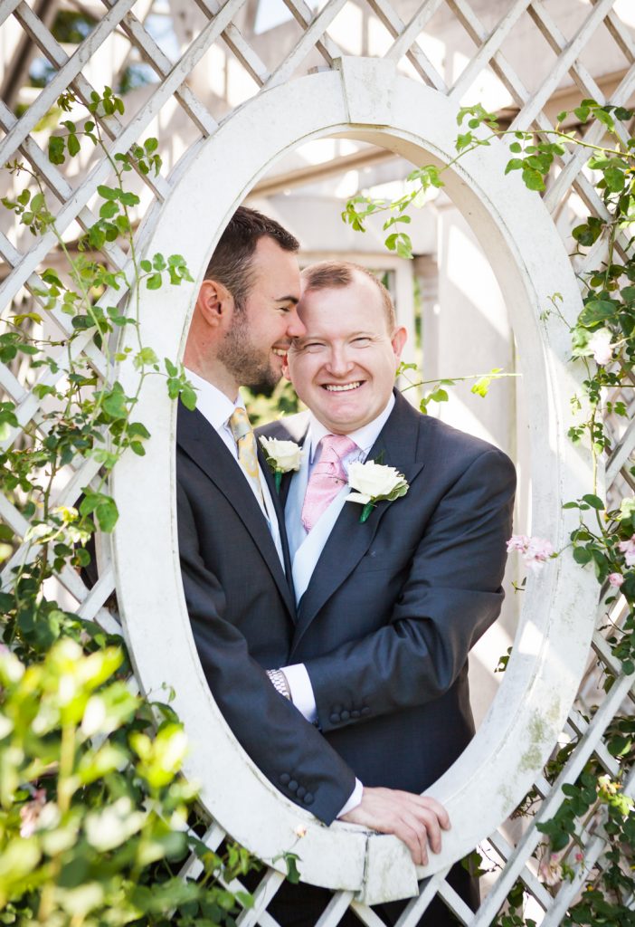 Two grooms looking out window of rose trellis at an Brooklyn Botanic Garden wedding