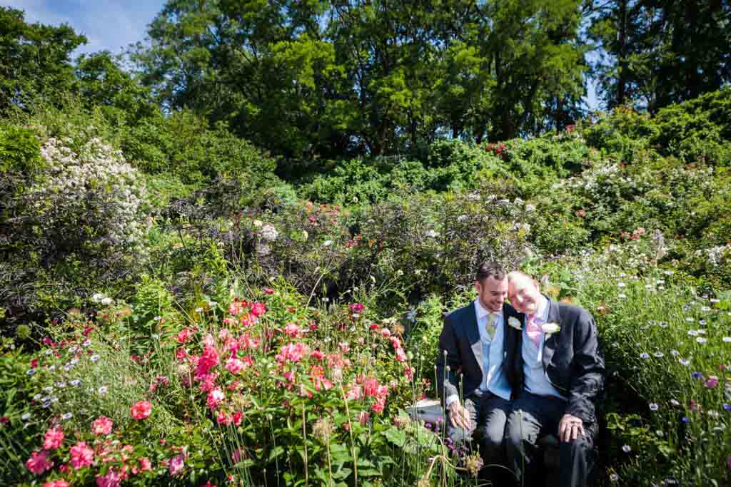 Two grooms sitting on bench in the middle of rose garden at an Brooklyn Botanic Garden wedding