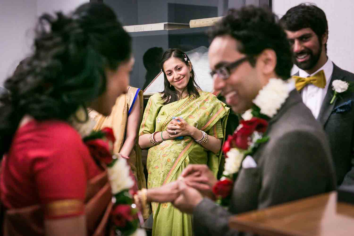 Woman wearing green sari watching groom put ring on bride's finger at a NYC City Hall Indian wedding