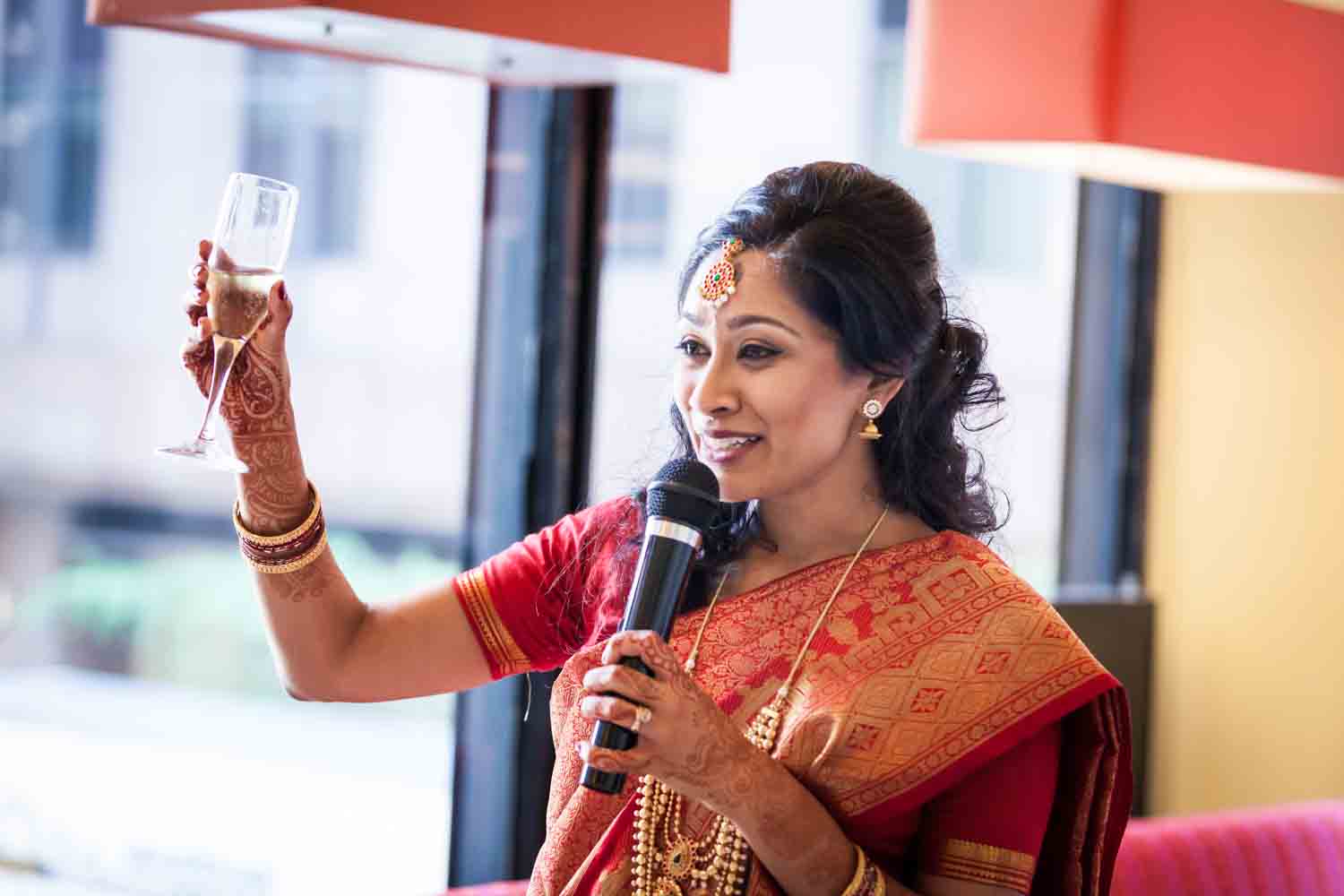Indian bride in red sari holding up champagne glass at a NYC City Hall Indian wedding