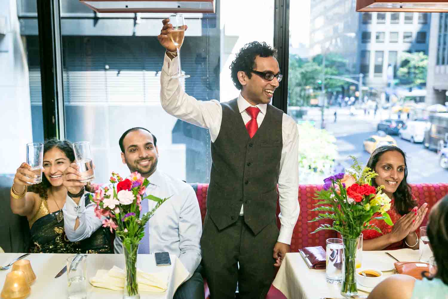 Groom standing between tables of guests holding glass of champagne