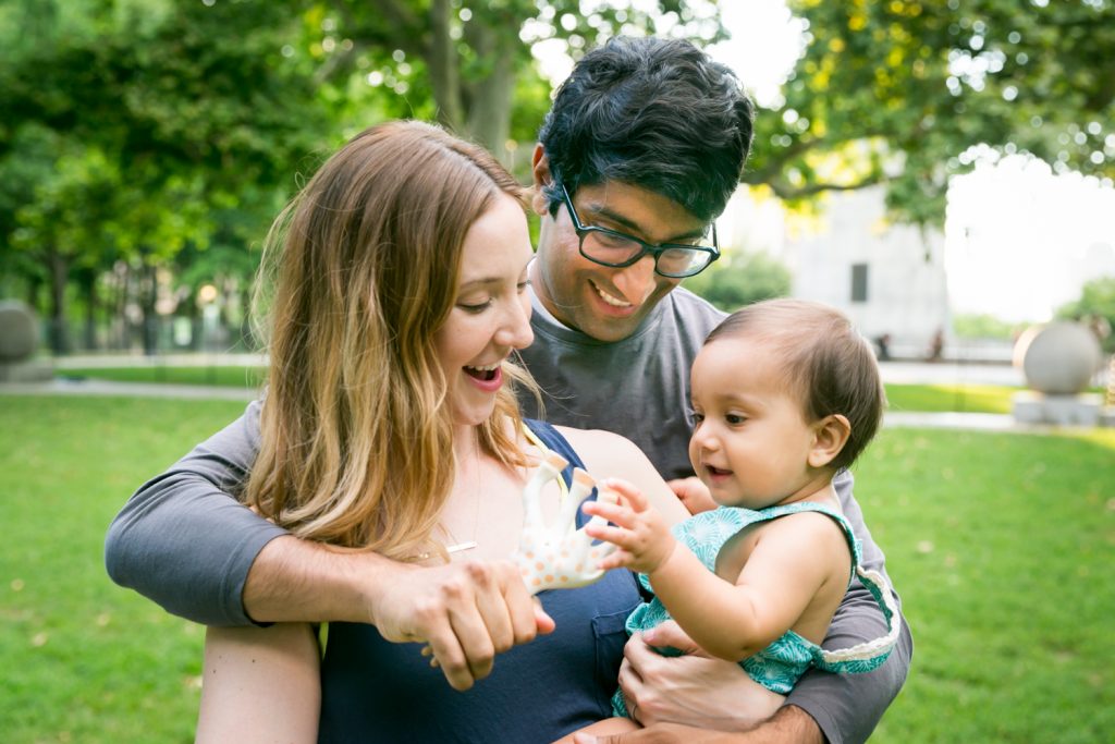 Little toddler playing with toy and her parents during Fort Greene Park family portrait
