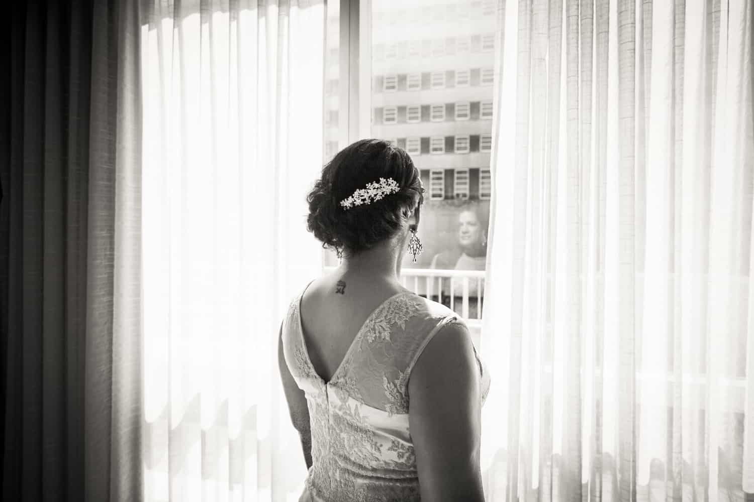Black and white photo of bride looking out of hotel window
