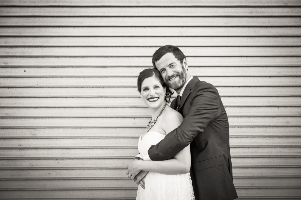 Black and white photo of bride and groom hugging in front of metal gate