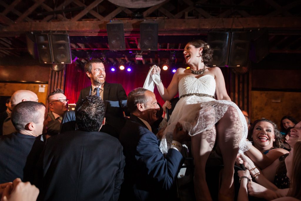 Bride and groom lifted on chairs during hora dance at a Bell House wedding anniversary party