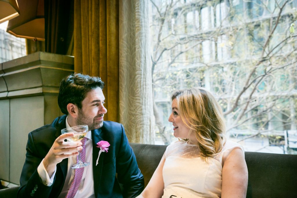 Bride and groom drinking champagne on a sofa by window in the Soho Grand Hotel