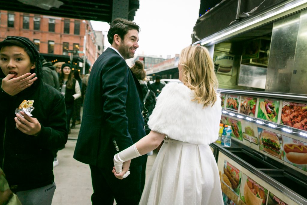 Bride and groom holding hands and walking past hot dog vendor